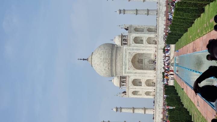 Frontal view of the Taj Mahal with reflecting pool and crowds of visitors lining the pathway