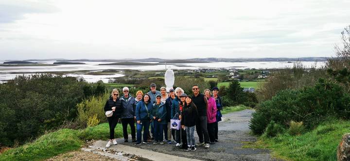 Tour group posing at a scenic overlook of Irish lakes and rolling countryside
