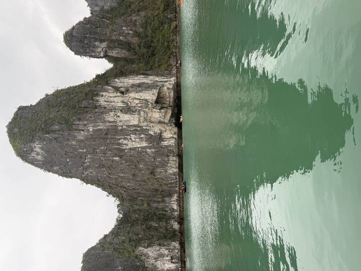 Tall limestone karst rises dramatically from the jade waters of Halong Bay, its reflection mirrored below