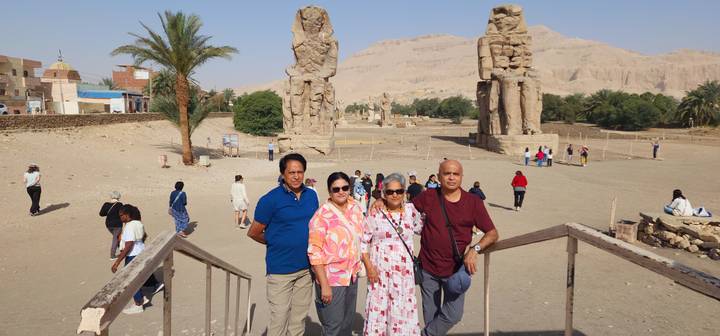 Travellers stand before the towering Colossi of Memnon statues with the Theban hills beyond.