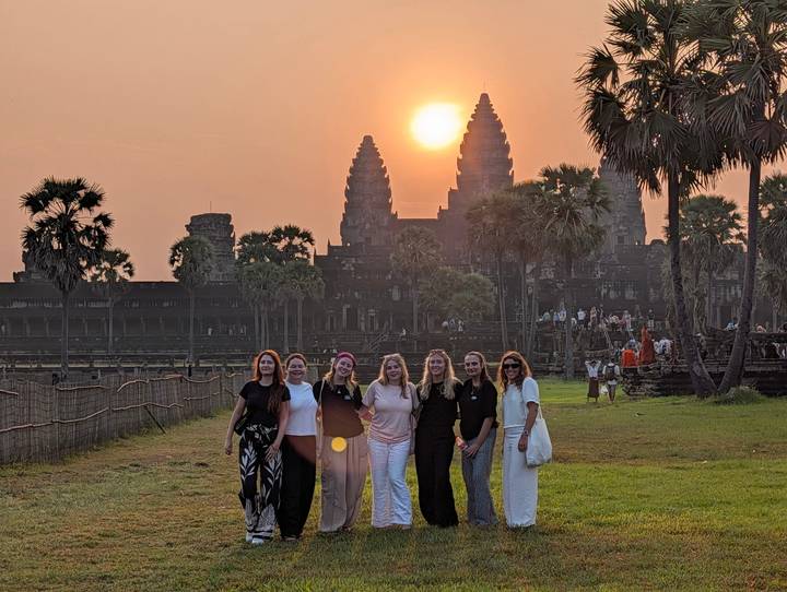 Group of travellers smiling at sunrise in front of Angkor Wat’s iconic towers.