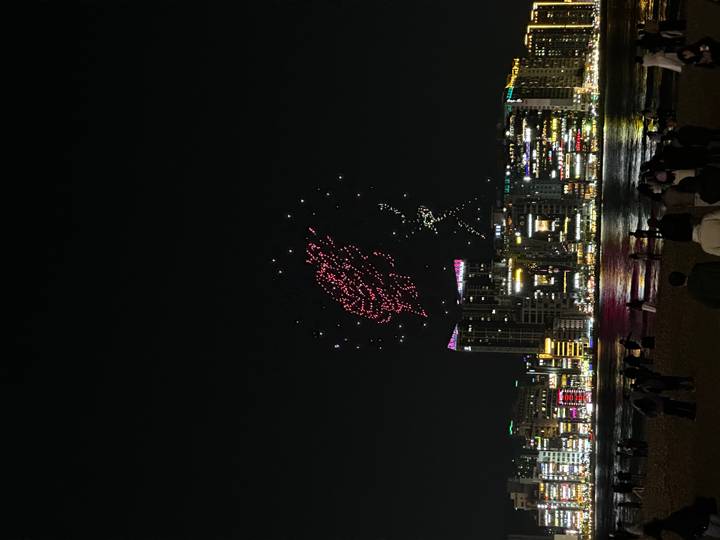 Nighttime drone and fireworks display above Busan skyline and beach with spectators