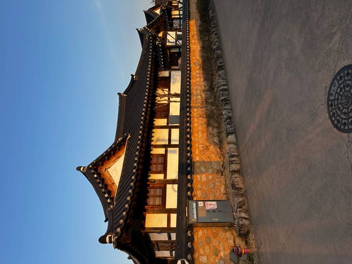 Traditional Korean hanok-style building with tiled roof and stone wall warmly lit by late afternoon sunlight under a clear blue sky.
