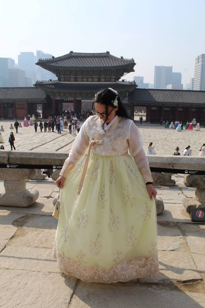 Woman wearing a pastel hanbok admiring her dress in the courtyard of a historic Korean palace.
