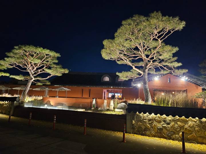 Cozy brick restaurant building illuminated by warm lights and flanked by sculptural pine trees at night.
