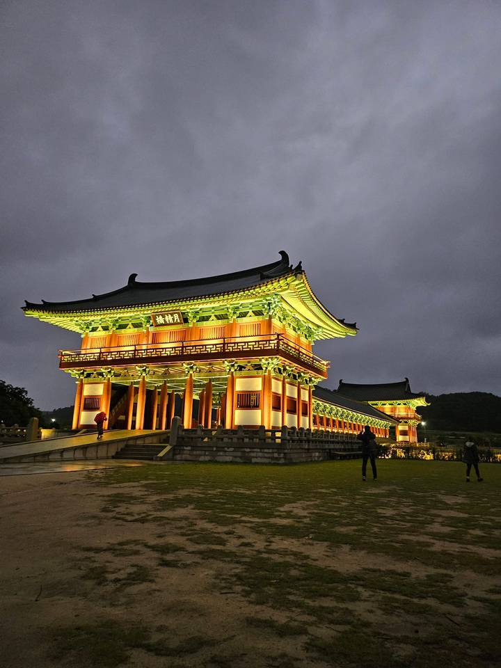 Grand traditional pavilion in Gyeongju glowing gold and green under evening lights against a moody sky.