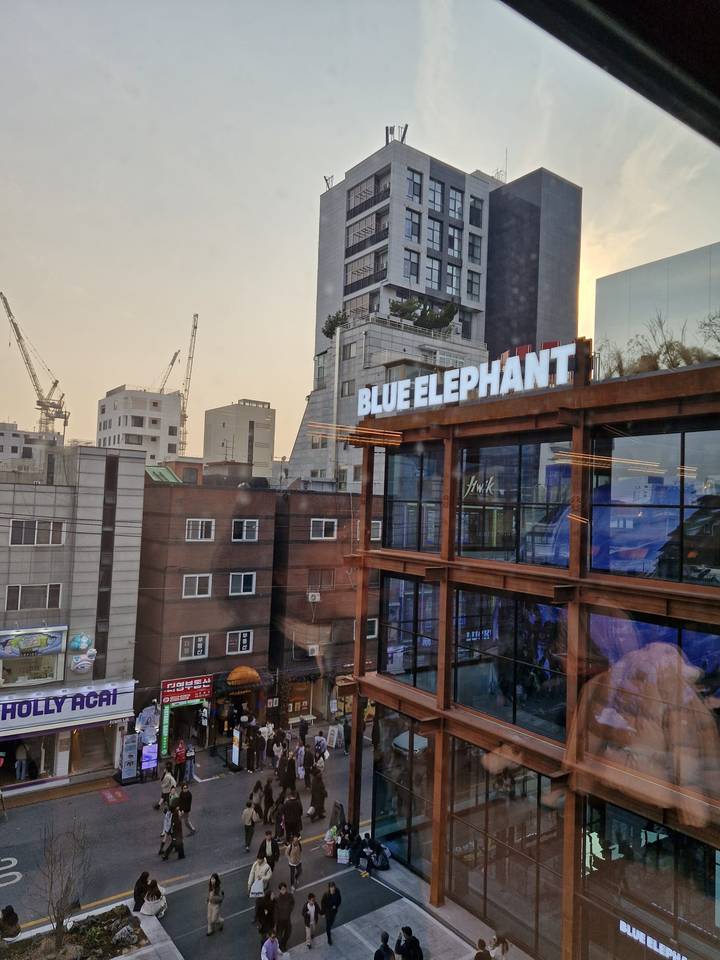 Cityscape at dusk with cranes and buildings reflecting in large windows of a ‘Blue Elephant’ venue.