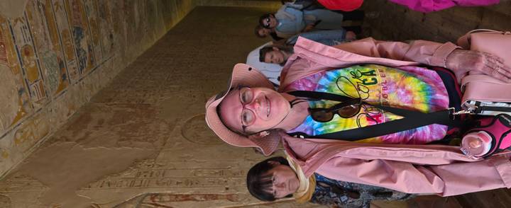 Smiling tourist in a tie-dye shirt stands inside a hieroglyph-covered corridor.