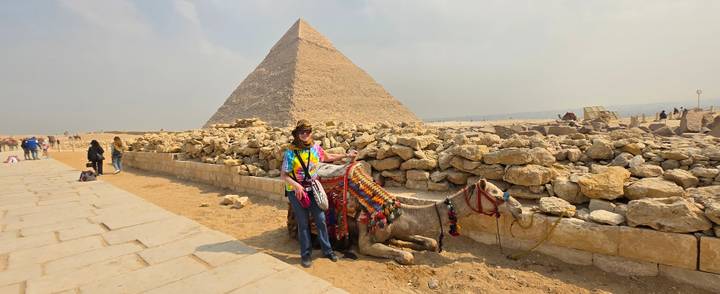 Traveler poses with a resting camel in front of the Great Pyramid of Giza.