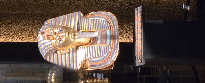 Glittering golden mask of Tutankhamun displayed in a museum case.