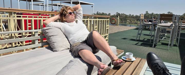 Woman lounges on a sunbed with coffee while cruising the Nile River.