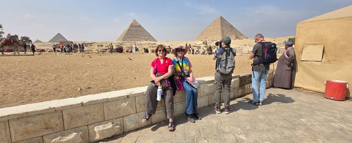 Travelers gather near the pyramids while another visitor photographs them.