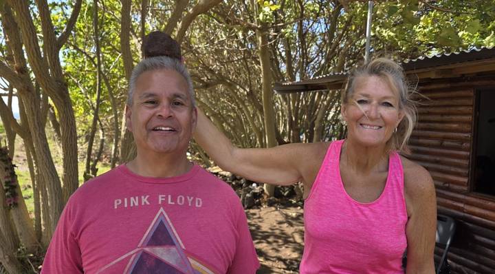 Smiling woman playfully rests a volcanic stone on a man’s head among coastal trees.