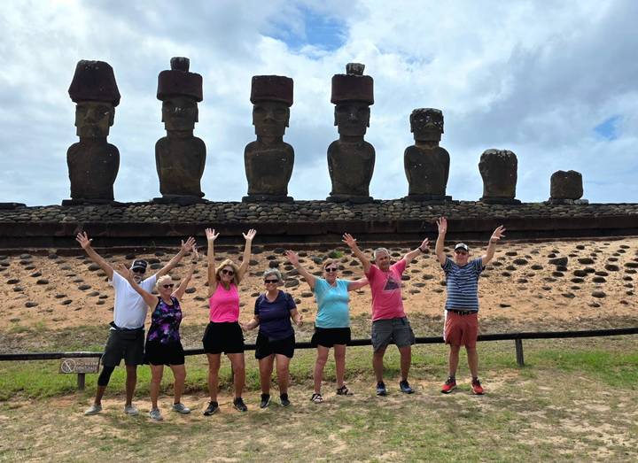 Tour group jumps with raised arms before a row of towering moai statues.