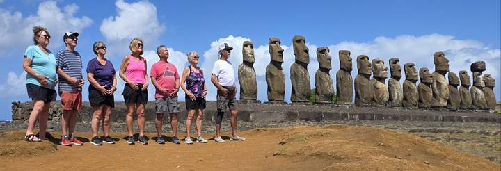 Visitors stand in line mirroring a long row of moai under a blue sky.