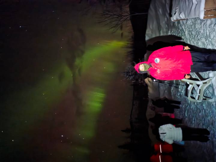 People watch colorful green aurora borealis dancing in the night sky over snow.