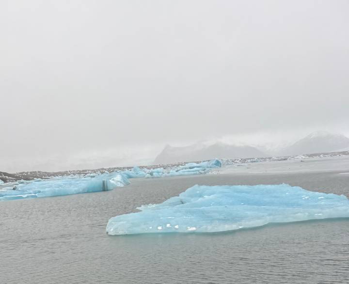 Pale blue icebergs floating in a misty glacial lagoon