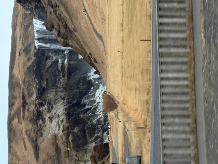 Distant view of Skógafoss waterfall cascading over a cliff into a rugged canyon in winter