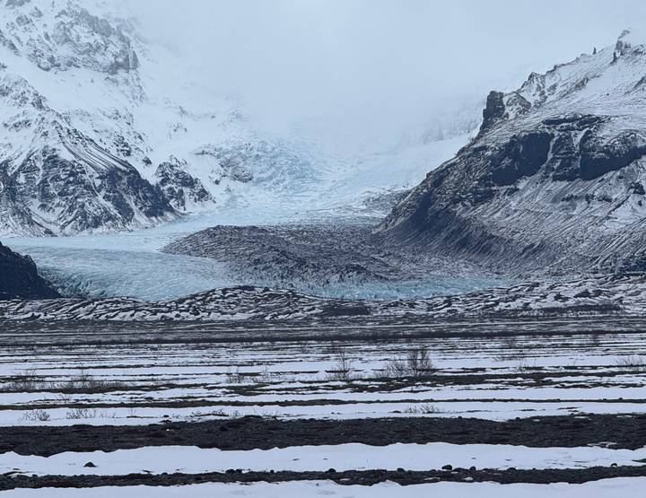 Expansive glacier tongue descending between snow-covered peaks and a snowy plain