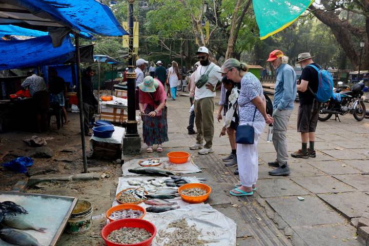 Visitors browse fresh fish laid on cloth at an outdoor street market stall.