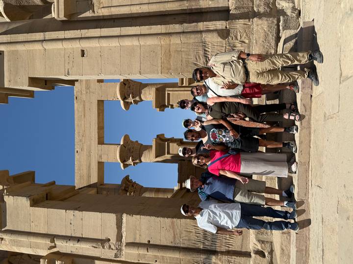 Tour group posing on steps in front of ancient columns at Philae Temple under a bright blue Egyptian sky.