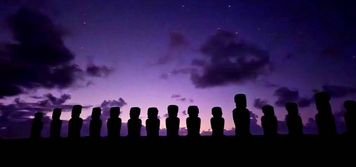 Silhouetted line of moai statues under a starry purple twilight sky on Easter Island.