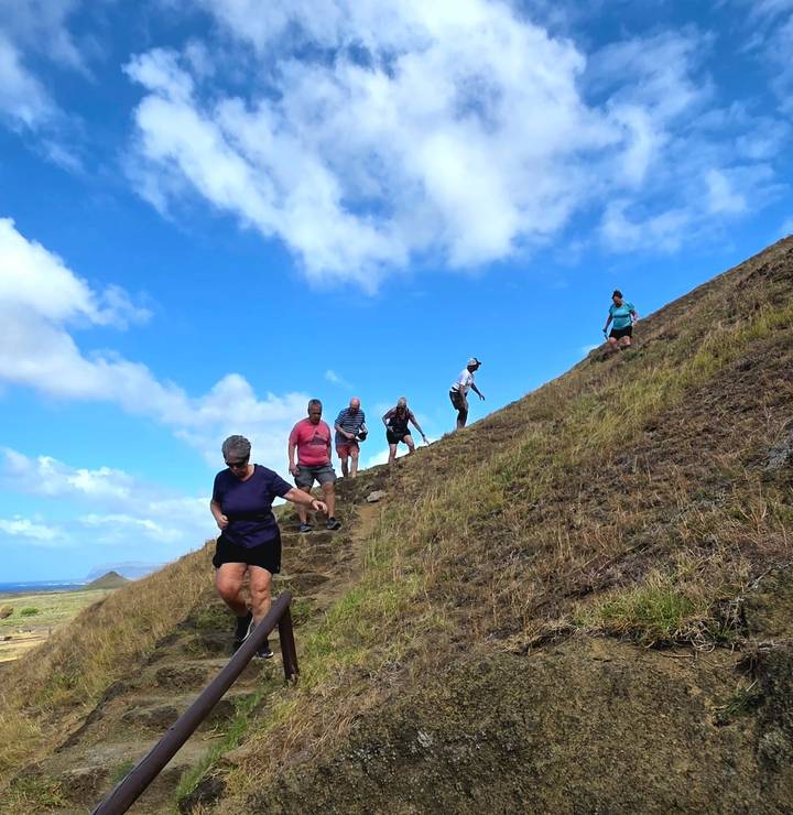 Hikers descending a grassy volcanic slope under bright blue sky on Easter Island.