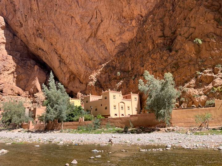 A traditional kasbah-style building nestles at the base of a massive red rock overhang in the gorge.