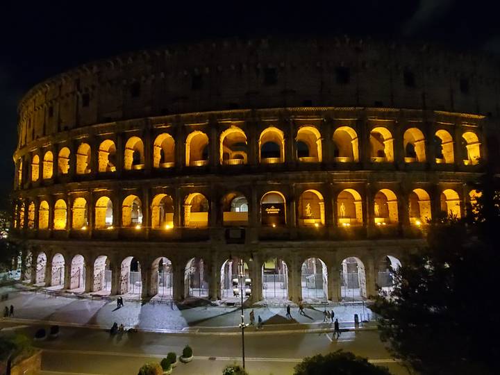 The Colosseum glows with golden illumination against the night sky, its ancient arches in sharp relief.