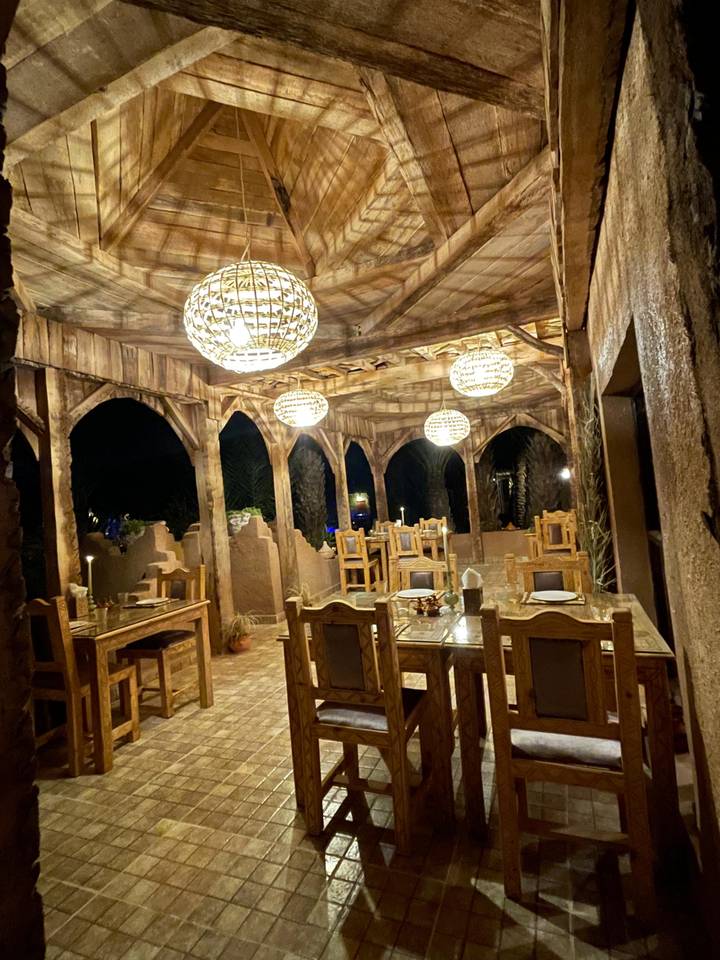 Rustic open-air dining area with wooden arches and hanging lanterns at night.
