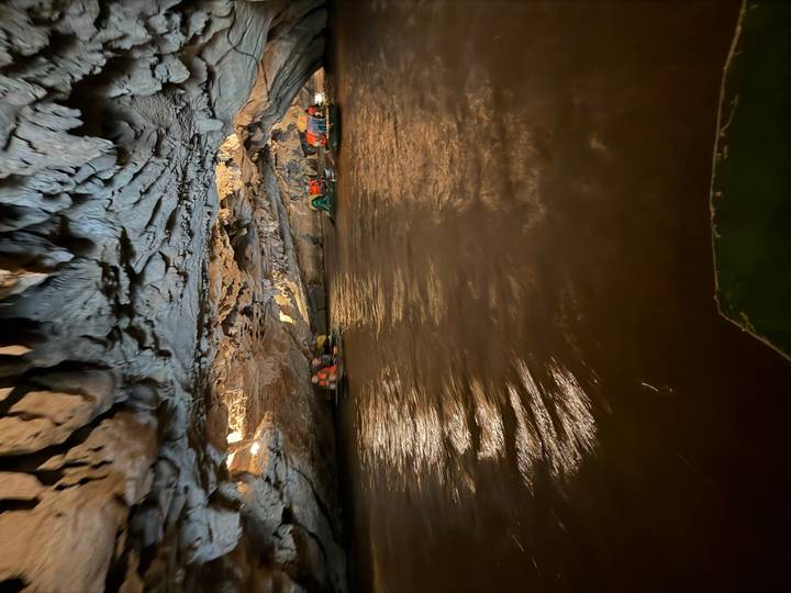 Low-lit boat passes through a cavernous limestone cave over dark water.