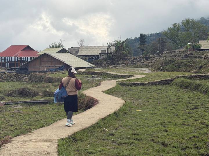 Young woman walks along a winding dirt path through rural terraced fields.