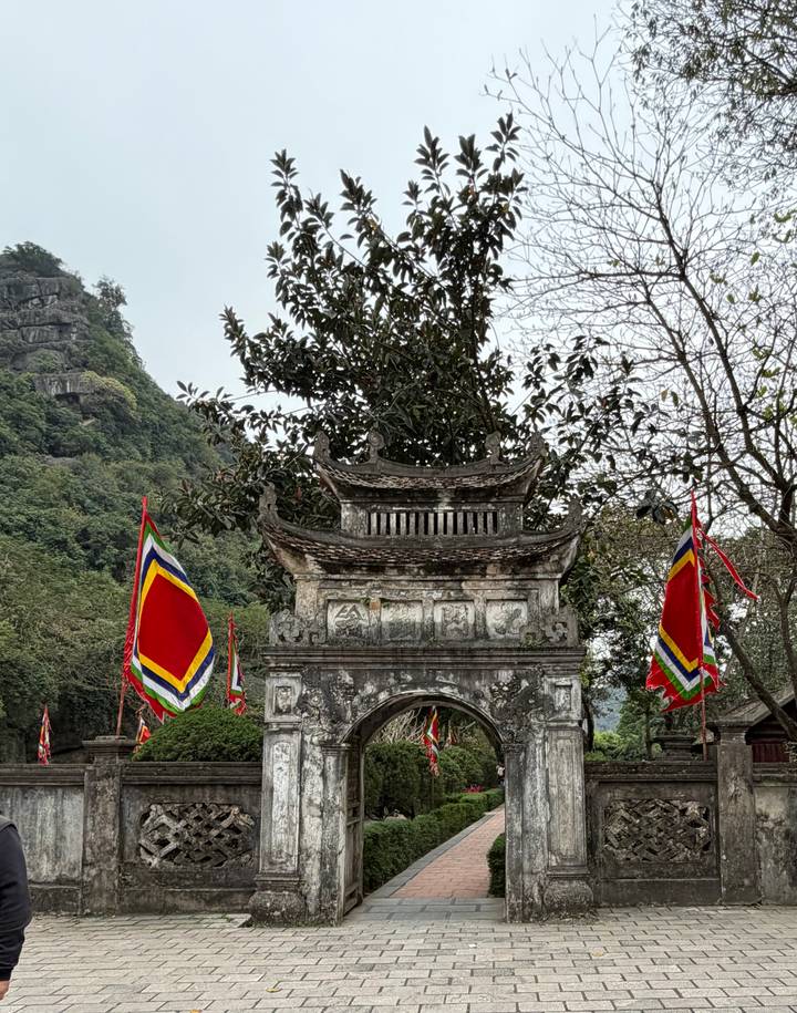 Ancient stone gate adorned with colorful flags set against lush cliffs.