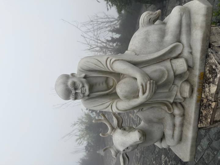 Marble statue of a seated monk beside a deer enveloped in dense fog.