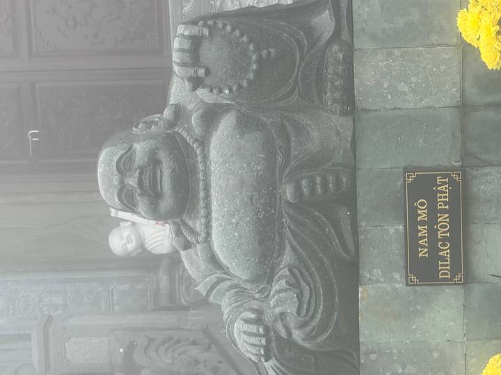 Large stone laughing Buddha statue partially shrouded in mist at a mountaintop temple.