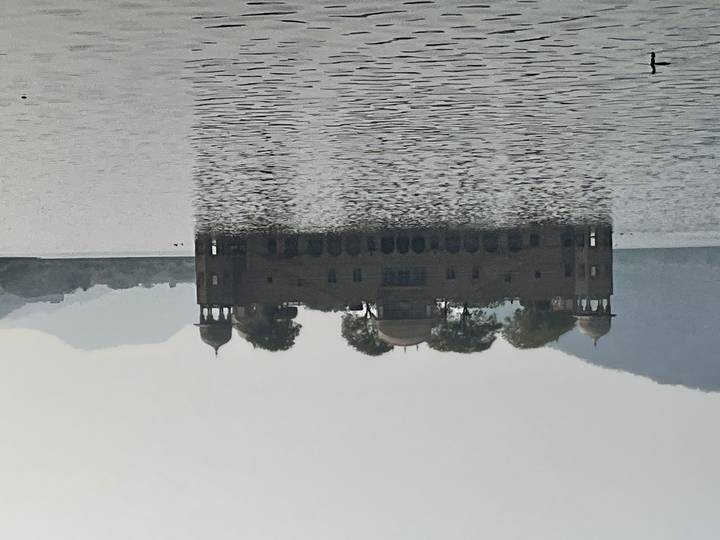 Hazy daylight view of the Jal Mahal water palace standing in the middle of a calm lake.