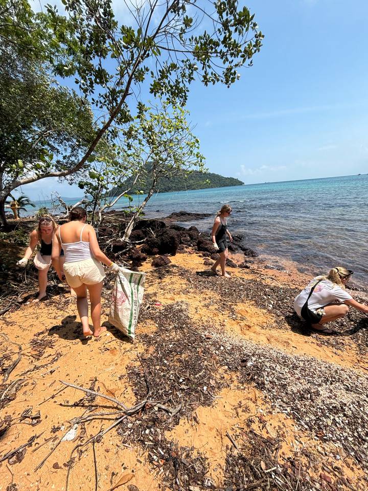 Travellers collecting rubbish along a tropical island beach beside turquoise water.