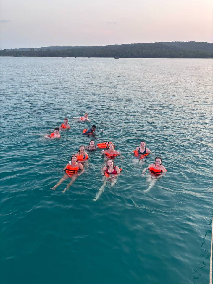 Smiling travellers wearing life jackets float together in clear blue sea water.