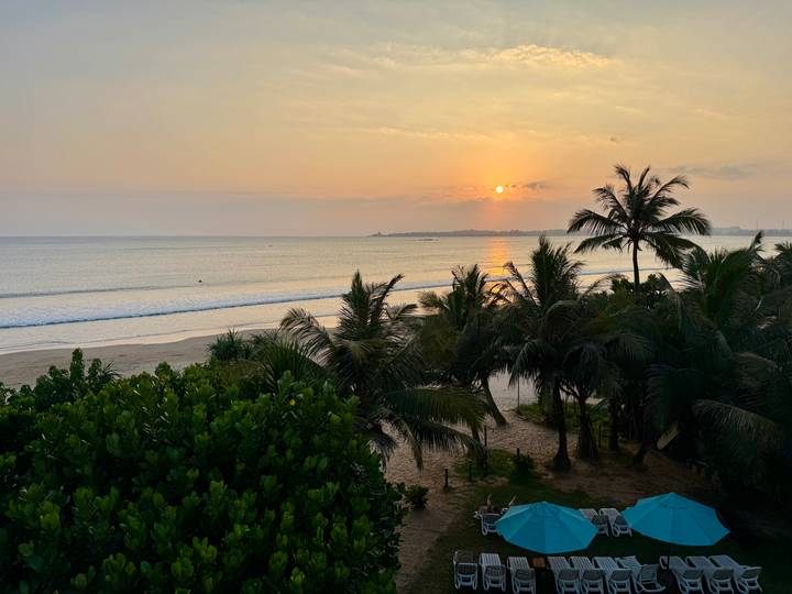 Soft sunrise over a calm tropical beach with palm trees and gentle waves reflecting the orange sky.