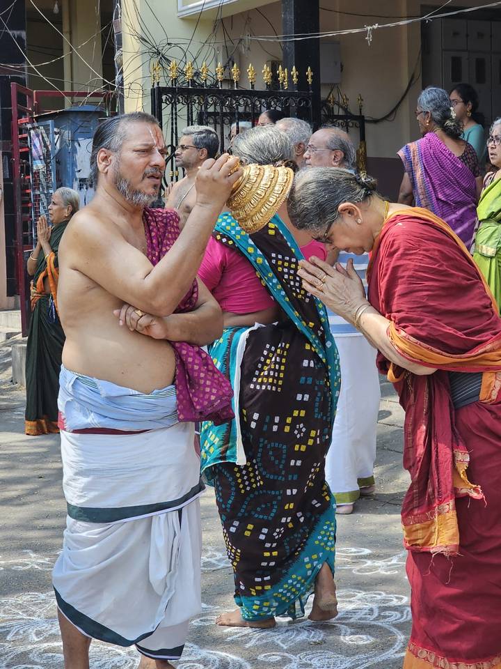 Traditional Hindu greeting as a woman bows with folded hands to a bare-chested priest in the street.