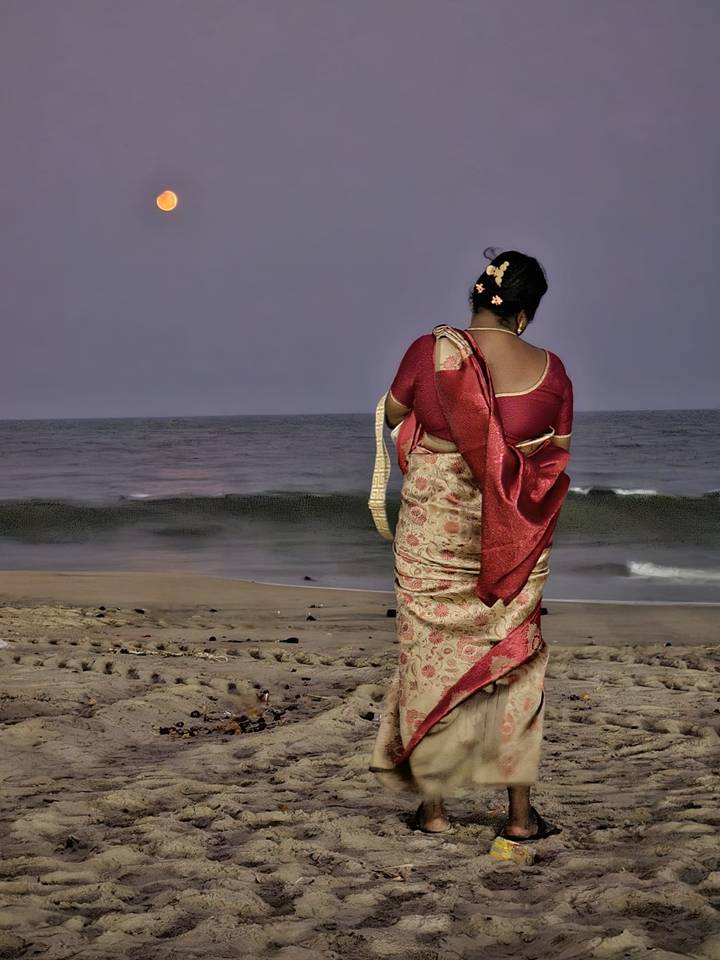 Woman in ornate sari gazes at the sea from a quiet beach at twilight.