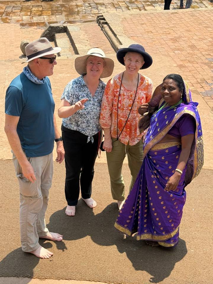 Travellers and guide pose on temple steps, the guide wearing a purple sari.