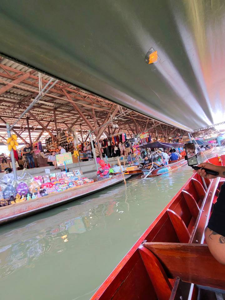 Bustling floating market scene viewed from a long-tail boat with stalls, souvenirs and paddling vendors.