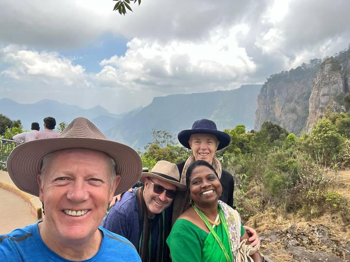 Smiling travellers pose at a misty mountain viewpoint with cliffs and deep valleys behind.