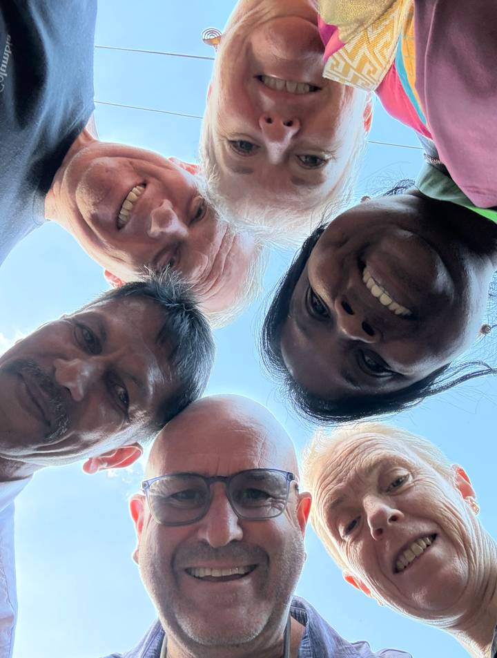 Circular face-in selfie of five travellers looking down at camera, similar to previous shot.