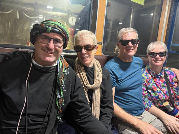 Travellers wearing sunglasses sit inside a vintage train carriage tunnel section.