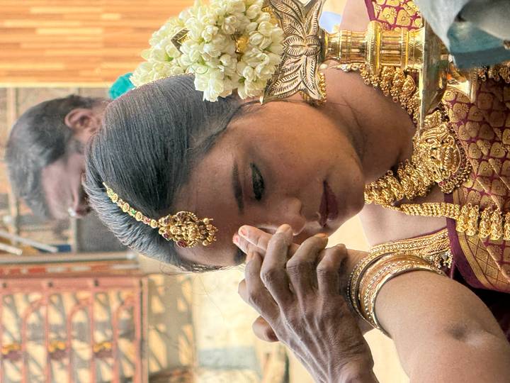 Close-up of bride having ritual mark placed on her forehead, adorned with ornate gold jewellery.
