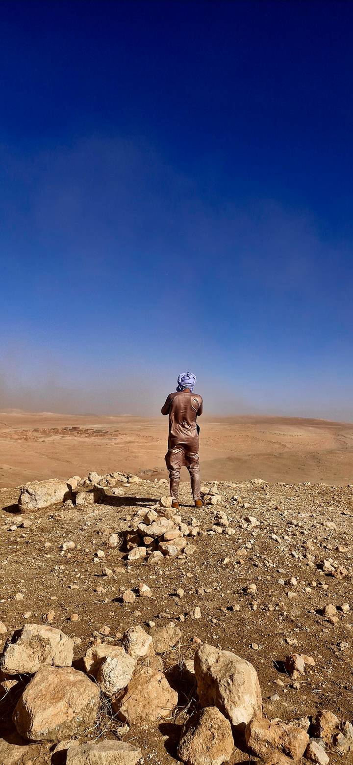 Traveller dressed in traditional robe gazing over vast desert panorama beneath clear blue sky