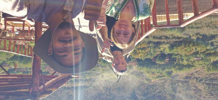 Three happy travellers giving thumbs up on a sunny terrace with valley backdrop and lens flare