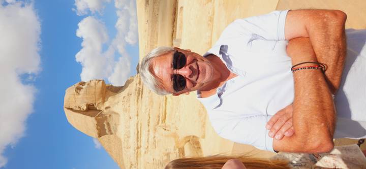Smiling tourist poses in front of the Great Sphinx under a bright blue sky